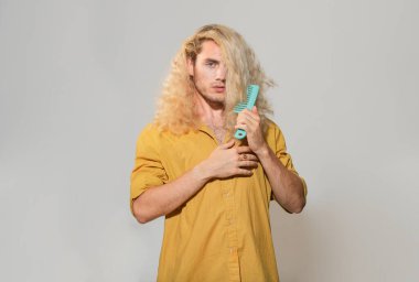 Saçlarını tarayan yakışıklı bir adamın portresi. Saç modelini kapat, erkek fırçası saç modelini al, gri arka plan ayır. Saç fırçalayan adam