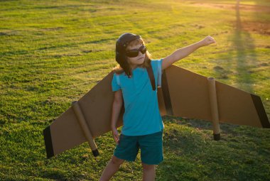 Sırt çantalı kanatlı çocuk gezgin. Pilot pilotçuluk oynayan ve dışarıda parkta rüya gören bir çocuk. Hayal, özgürlük ve seyahat konsepti