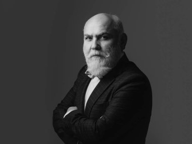 Kollarını kavuşturmuş kıdemli adam. Belden yukarı portre. Sakallı, orta yaşlı, ciddi bir yüz ifadesi olan, yakın plan bir kafa ve omuz portresi olan adam.