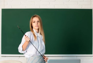 Genç ciddi öğretmen dersi işaret ediyor. Kara tahtanın yanında işaretçi öğretmenliği yapan sevimli genç bir kadın.