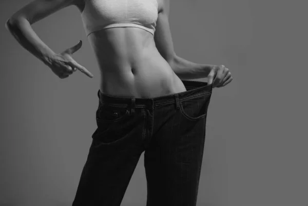特大のジーンズで食事のコンセプト 大きすぎるジーンズの痩せた女性 成功した減量の概念 細い女の子で大ズボンでグレーの背景 — ストック写真