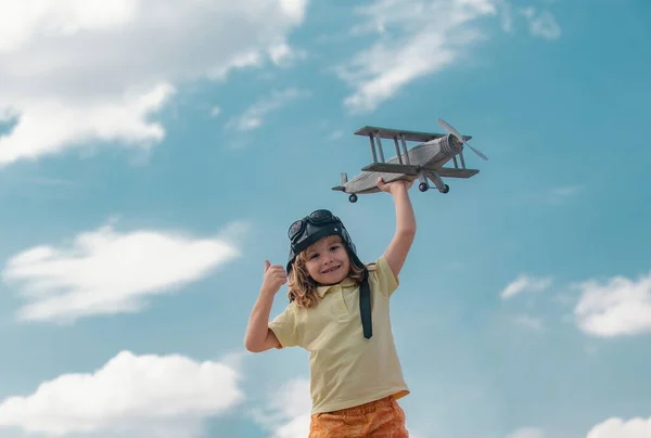 Child boy with pilot goggles and helmet playing with wooden toy airplane, dream of becoming a pilot. Childrens dreams. Child pilot aviator with wooden plane. Summer at countryside