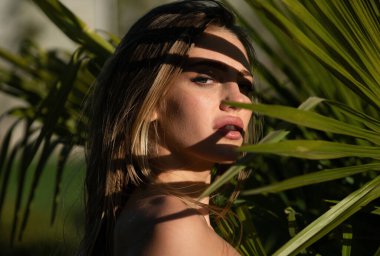 Sağlıklı cilt ve palmiye yaprakları olan genç ve güzel bir kadın. Çekici bir kızın yeni yüzü. Yaz modeli, egzotik tropik kozmetik