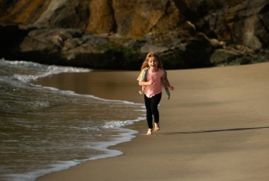 Sahilde oynayan çocuklar. Çocuklar yaz tatilinde denizde oynarlar. Kum ve su eğlencesi, güneş koruması. Eğitimdeki küçük bir atlet. Koşucu spor yapıyor, çocuklar için koşuyor.