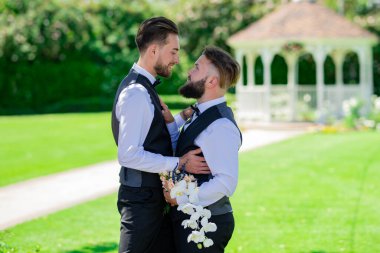 Düğün günü partneri olan eşcinsel bir adam. Evli LGBT çiftleri romantik bir düğün törenini bir buket çiçekle kutluyorlar. Düğün gününde birbirine aşık eşcinsel bir çiftin portresi. Neşeli düğün açık havada