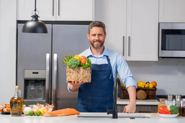 コック エプロンのシェフだ 現代のキッチンの男は 単独で健康的な食べ物を準備し サラダを調理します ハンサムな男は自宅でキッチンで新鮮なビーガンサラダを準備しています 健康食品は健康的な生活です — ストック写真