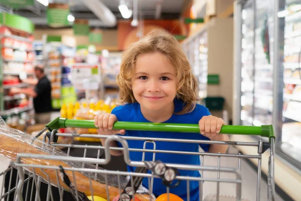 Kid with shopping cart at grocery store. Kid on shopping in supermarket. Grocery store, choosing goods. Shopping for healthy