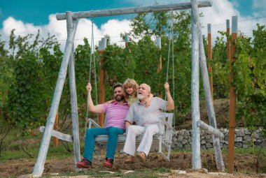 Aile Erkekler Hafta Sonu. Üç nesil boyunca birlikte, gülümseyen oğul, baba ve büyükbaba salıncakta sallanıyor, parkta eğleniyorlar.