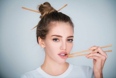 Seksi, şehvetli bir kadın, elleri yemek çubuklarını seksi dudaklarının yanında tutuyor. Çin ya da Japon yemekleri, suşi reklamları.