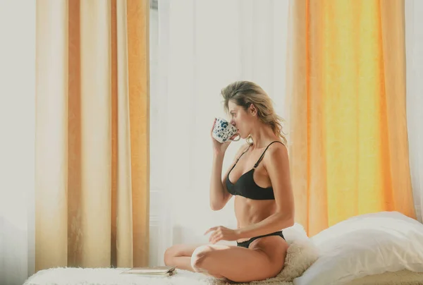 床上放着咖啡杯的金发女人年轻健康的女孩在卧室里 早上喝咖啡 — 图库照片