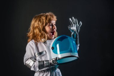 Uzay giysisi içinde, siyah arka planda miğfer tutan sevimli küçük bir uzaylı çocuk. Astronot kostümü giymiş bir çocuk astronot olma hayalleri kuruyor.