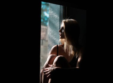 Pencerenin yanında şehvetli bir kız. Gölgedeki kadın. Yüzünde gölgeler olan kadın model. Işıklı dramatik siyah stüdyoda baştan çıkarıcı ve şehvetli görünüyor.