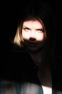 Stüdyoda poz veren genç bir kadın. Işık ve gölge. Yüzünde koyu renk ışık olan güzel bir kadının moda portresi. Kadınların yüzüne gölge ve ışık yansıtan yaratıcı portreler, gözler