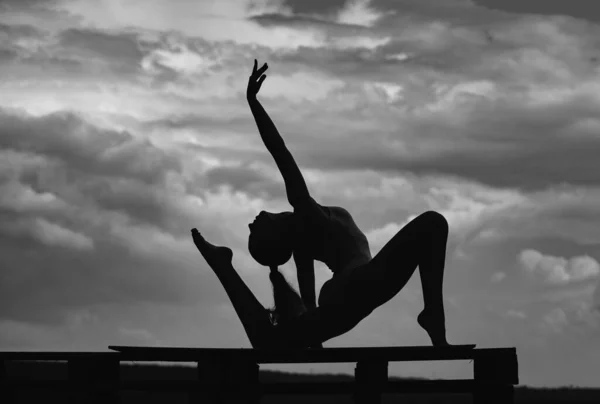 瑜伽女子伸展与姿势伸展 健美运动员女子运动伸展的轮廓 多云的天空背景 — 图库照片