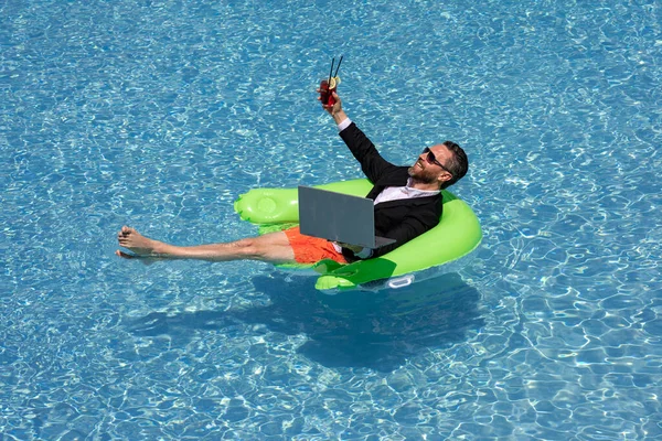 Crazy summer. Business drink summer cocktail and using laptop in suit in water pool. Fun business lifestyle. Funny businessman dreams about summer. Freelance concept, summer travel. Business success