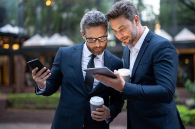 İş ortakları kahve molasında tablet kullanıyor, dışarıda buluşuyorlar. İş ortakları açık havada konuşur. Takım elbiseli iki yakışıklı iş adamı şehre karşı yürütülen bir projeyi tartışıyor.