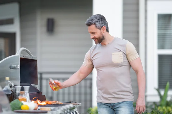 バーベキューのコンセプト バーベキュー用のTシャツを着た中年のヒスパニック系男性 ローストやグリル料理 肉を屋外で焙煎する バーベキューとグリル 裏庭で肉を調理 — ストック写真