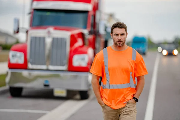Men driver near lorry truck. Man owner truck driver in safety vest near truck. Handsome middle aged man trucker trucking owner. Semi trailer, semi trucks. Handsome man posing in front of truck