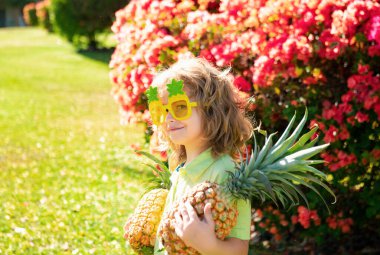 Ananas tutan ve arka bahçede gülümseyen komik çocuk. Ananaslı çocuk. Çocuklar yaz meyvesi