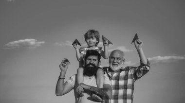 Baba ve büyükbabasıyla birlikte mavi gökyüzü arka planında parkta eğlenen genç bir çocuk. Babalar Günü - Büyükbaba, baba ve oğul kucaklaşıyor ve birlikte eğleniyorlar.