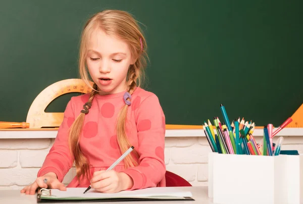 在校女生在黑板背景的课堂上做作业 小学时 小学生坐在课桌前 在笔记本上写字或画画 — 图库照片