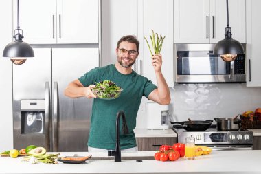 Çekici bir adamın portresi mutfaktaki evde taze kilo kaybı yemeği hazırlıyor. Yakışıklı neşeli adam mutfakta yemek hazırlıyor. Sağlıklı yiyecekler, yemek pişirme konsepti