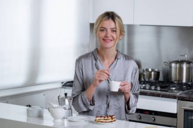 Gülümseyen mutlu kadın mutfakta kahve içer. Sabahları seksi ev hanımı