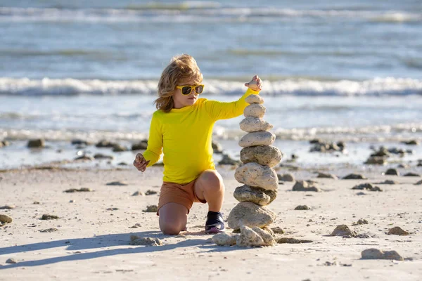 夏の子供の瞑想 ビーチの砂の上でピラミッド型の石のバランスで遊ぶ小さな子供 海に石の山を持つ子供 子供はビーチで石のバランスで遊ぶ バランスと調和 — ストック写真