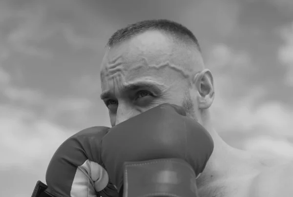 Boxer in a fight. Fist fight. Strong man strong body boxing outdoor. Man with muscular body and bare torso with boxing punch gloves. Man face close up in boxing