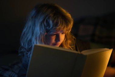 Çocuk yatakta sihirli bir kitap okuyor. Çocuk evde kitap okurdu. Uyku masalı, çocuk masalı.