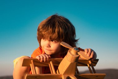 Tahta oyuncak uçakla oynayan çocuk pilot olma hayali kuruyor. Çocuk rüyaları. Ahşap uçaklı çocuk pilot. Tatlı çocuk suratı.