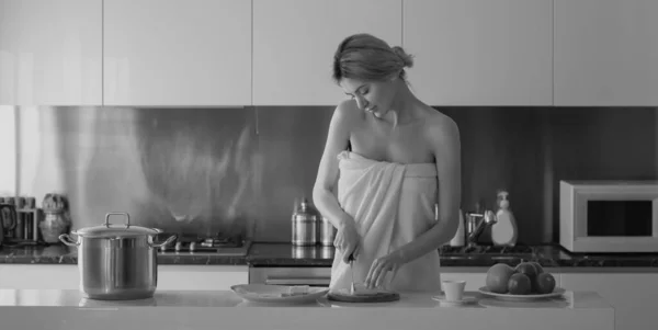 年轻女人做早餐 早上在家里性感瘦小的女人 在厨房做早餐的时候 穿着浴巾 光着肩膀的漂亮性感女性家庭主妇站在厨房里 — 图库照片