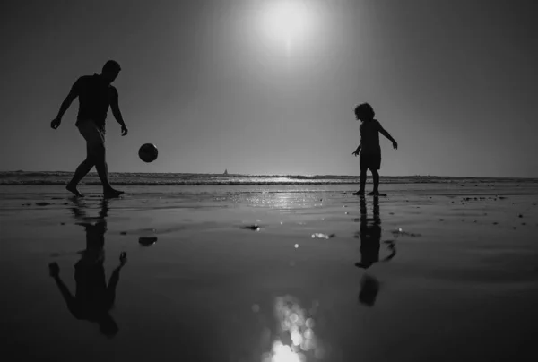 父と息子はビーチでサッカーやサッカーをしたり 日没のシルエットをしたりします 父と子供は屋外で楽しんでいます — ストック写真