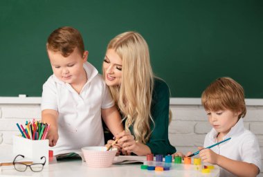 Öğretmen okuldaki öğrencilere yardım ediyor. Anaokulunda çizim yapan çocuklar