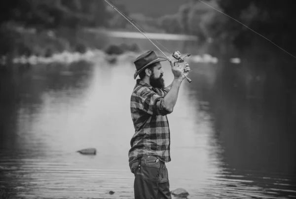若い男釣り ロッドを持つ漁師 川の岸にリールを回転させます 湖で釣りをしながらロッドを引く魚を捕まえる男 野生の自然 釣り趣味と春の週末 — ストック写真