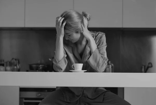 Depressed woman in the kitchen in the morning. Upset woman sitting in the kitchen watching phone in the morning and chatting smartphone. Sad tired housewife
