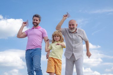 Çocuklarla aktif aile eğlencesi. Oğlu babası ve büyükbabası ile oyuncak uçağıyla yaz gökyüzü arka planında oynuyor. Seyahat konsepti. Çocuk büyüyor, oğul büyüyor.