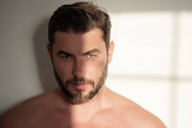 Yüz kreminden sonra tatmin olmuş genç bir adamın yakından güzel portresi. Çekici esmer adam tenine dokunuyor. Sakallı ve modern saç kesimli erkek modeller. Erkek kozmetik ve güzellik konsepti