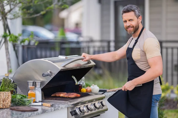 裏庭のグリルでハンサムな男バーベキュー 屋外やアメリカのライフスタイルのコンセプトを調理 バーベキューの肉を準備するハンサムな男 屋外での食事と料理の概念 — ストック写真