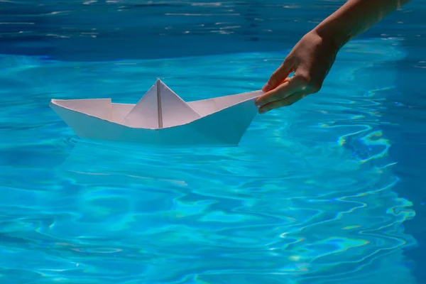 Hand is launching a white paper boat into the clear sea water. Tourism and traveling, travel dreams vacation holiday, sailing adventure