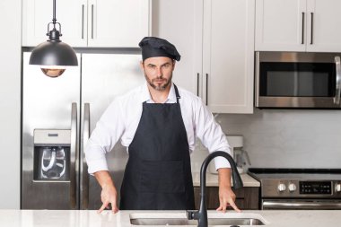Mutfakta şef şapkası takmış şefin portresi. Önlük, şef üniforması ve aşçı şapkası takan bir adam. Karakter mutfakçısı, reklam şefi.