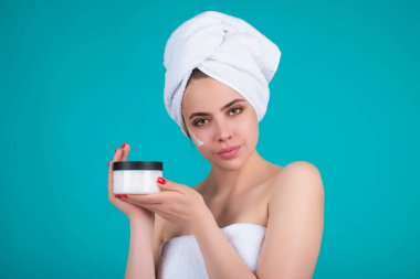 Beautiful model applying cosmetic cream treatment on face. Facial treatment. Beauty portrait of young topless woman with bare shoulders applying face cream