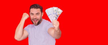 Nakit parayı dolar banknotlarıyla gösteren bir adam. Kırmızı stüdyo arka planında izole edilmiş bir iş adamı portresi. Başarılı bir kazanan ya başarıyı ya da zaferi para ile kutluyor. Kırmızı bayrak