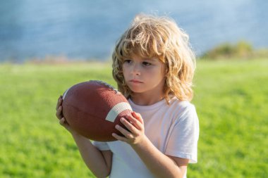 Yeşil çimen parkında Amerikan futbolu oynayan sevimli bir çocuk.