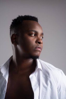 Altı paket düğmesiz kareli gömlekli Afrikalı siyahi adam modeli, kumsal kayaları, kum ve mavi gökyüzüne karşı izole edilmiş.