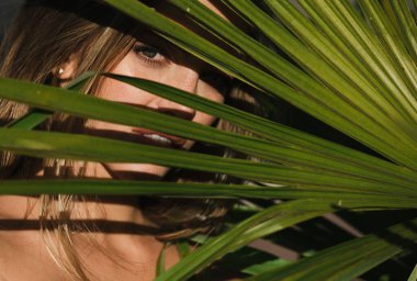 Tropikal palmiye yaprağından çıkmış narin bir kadının portresi. Güzel yüz, yakın plan.