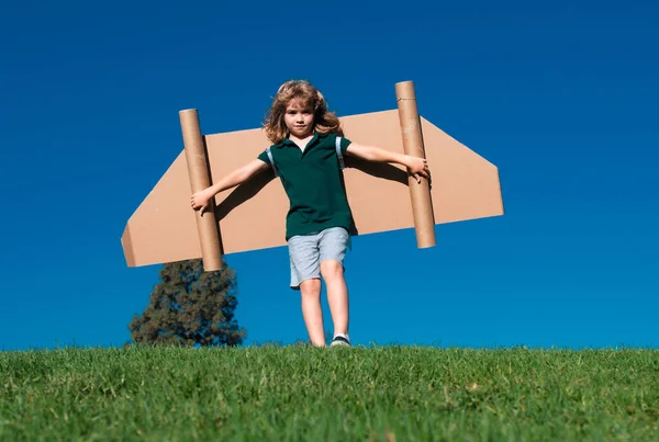 緑の芝生と青空で外で遊んでいる幸せな子供 おもちゃのジェットパック付きの子供パイロット おもちゃの飛行機の段ボールで子供の男の子の遊び 夏の旅行と冒険 成功者 想像力 夢のコンセプト — ストック写真