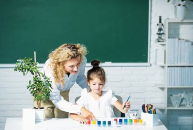 Okula dönelim. Anne ve kızı birlikte resim yapıyorlar. Öğretmen kıza yardım ediyor.