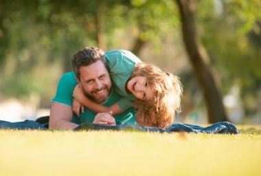 Baba ve çocuk dışarıda kucaklaşıp sarılıyorlar. Baba ve oğul yaz parkında çimlere uzanmış dışarıda vakit geçiriyorlar.