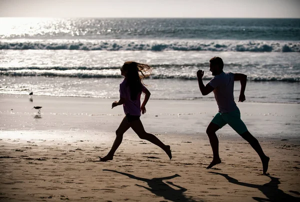 スポーツと健康的なライフスタイル 友人はビーチで日没でジョギング シルエットカップルビーチで実行しています — ストック写真